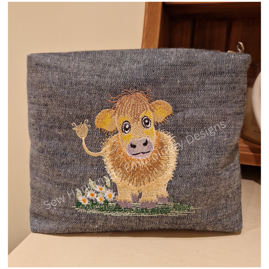 Machine embroidery design of a cute & fluffy Jersey cow with little daisy flowers and standing on a patch of green grass - stitched onto a denim zipper bag / pouch - instand digital download
